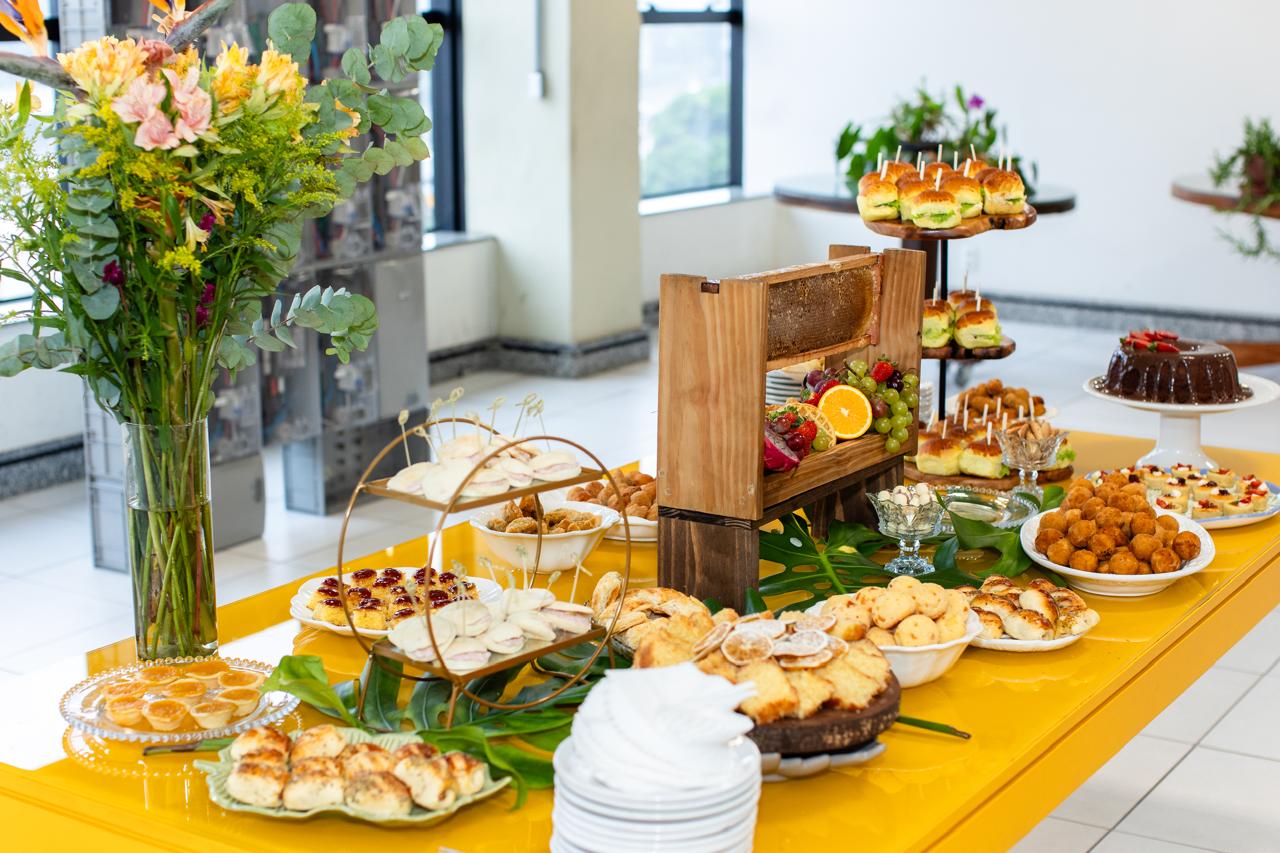 Mesa amarela com doces, salgados e mesa de frutas